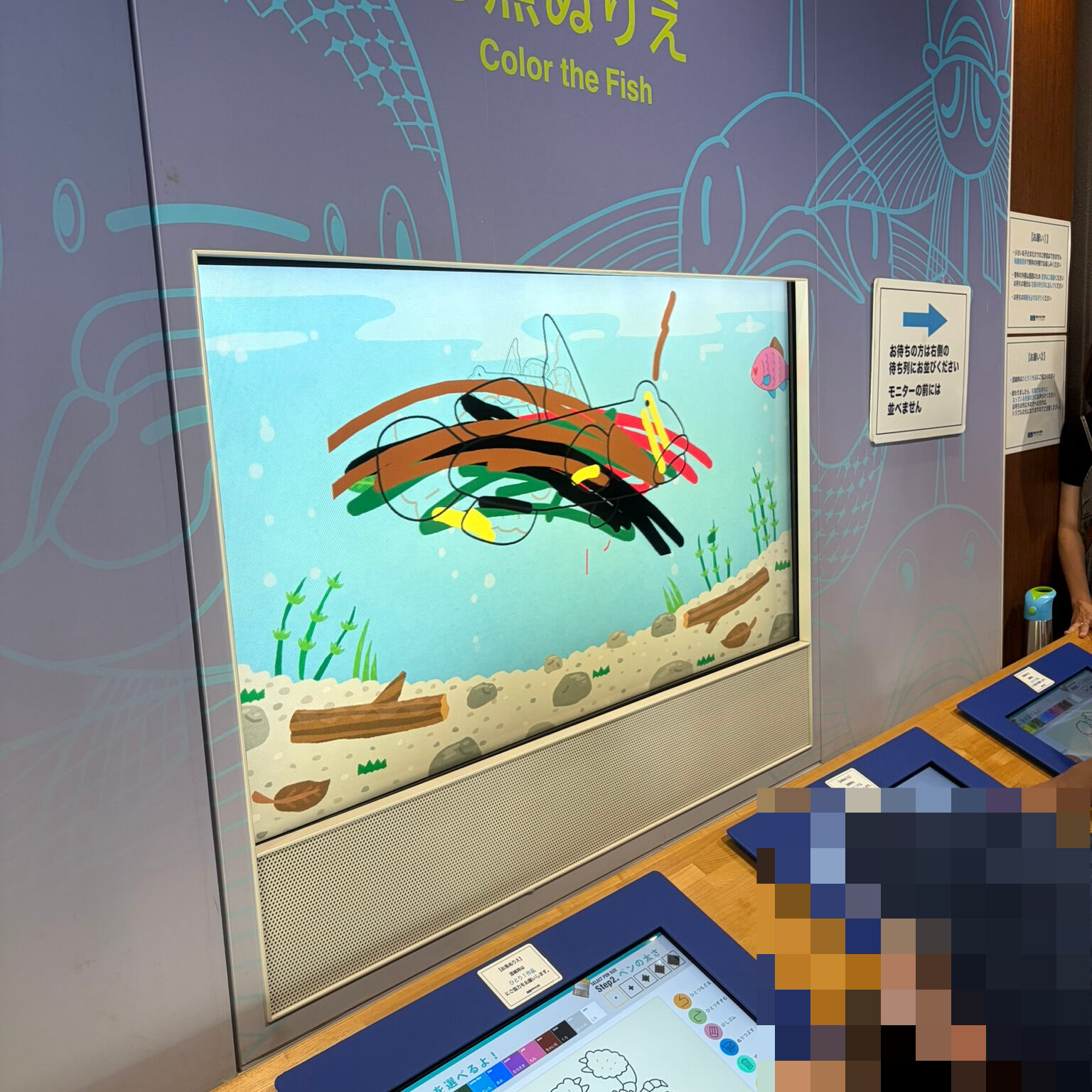 お魚塗り絵コーナーで色塗りをした画像が大きなスクリーンに映されている写真